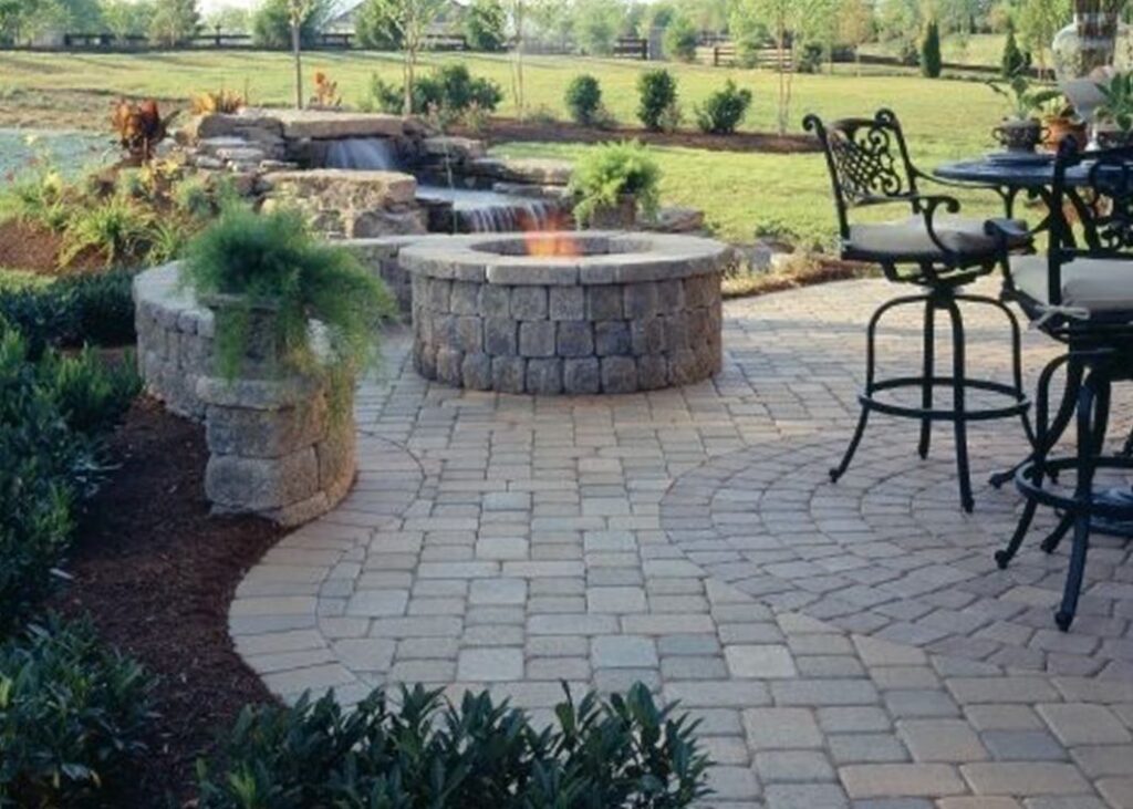 Outdoor fire pit installed on paver patio in front of water feature