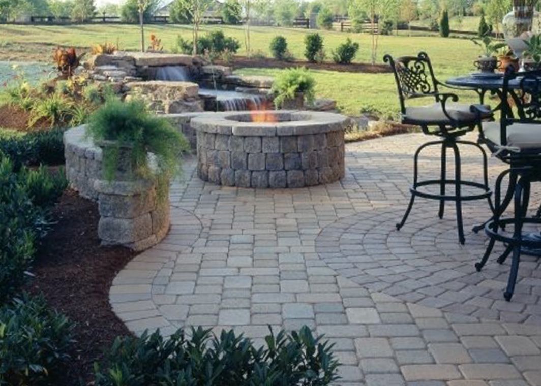 Outdoor fire pit installed on paver patio in front of water feature